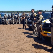 Fileira de policiais com as viaturas atrás e ao fundo a paisagem natural.