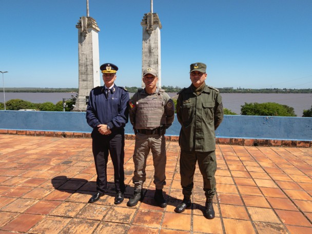 As autoridades policiais estão em pé e ao fundo vê-se o rio Uruguai. 