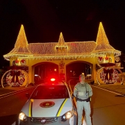 PM aparece ao lado de uma viatura em frente ao pórtico de entrada do município ue está todo decorado com as luzes de Natal.