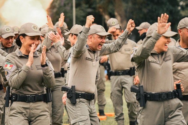 Momento de comemoração dos PMs ao final da solenidade de formatura no campo do estádio; batem palmas, vibram e sorriem.   