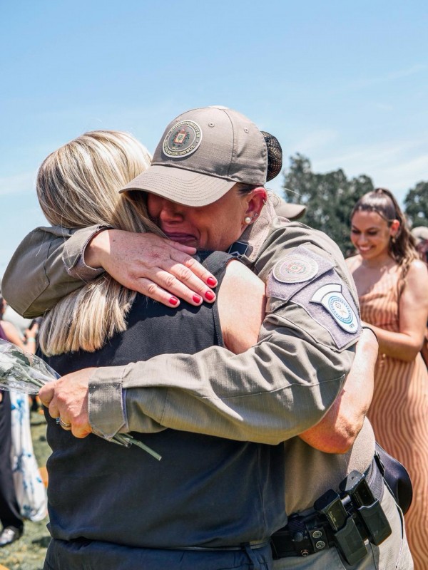 A PM formada chora e abraça a madrinha. 