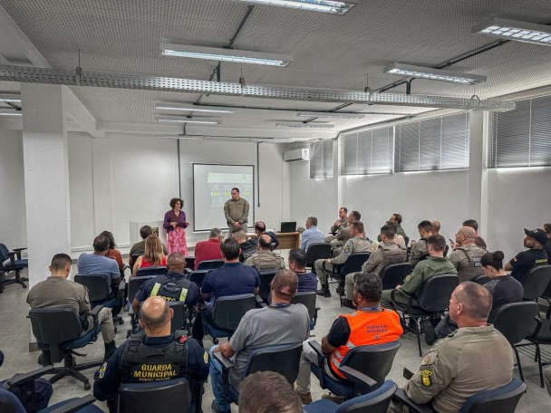 A Sala aparece lotada de policiais e duas pessoas aparecem diante do público. Atrás da dupla, há um quadro  com imagens do plano estruturado. 