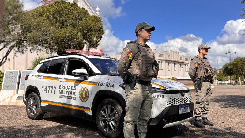 Dupla de PMs aparece em posi&ccedil;&atilde;o de sentido diante de uma viatura em um posto-base. 