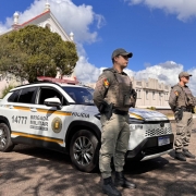 Dupla de PMs aparece em posi&ccedil;&atilde;o de sentido diante de uma viatura em um posto-base. 