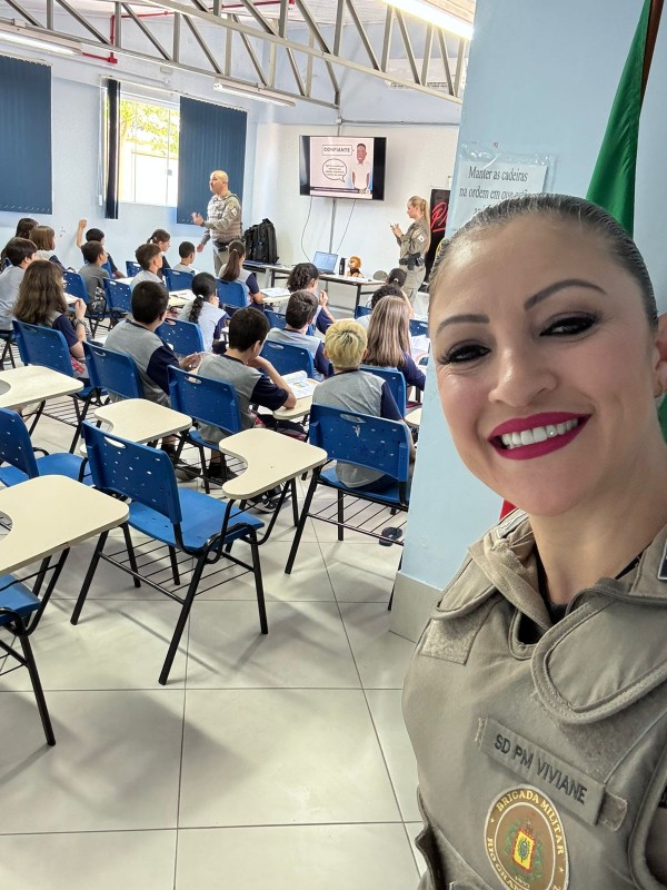 PM Viviane faz uma selfie mostrando os estudantes de costas ouvindo a dupla colega PM que ministra uma aula. 
