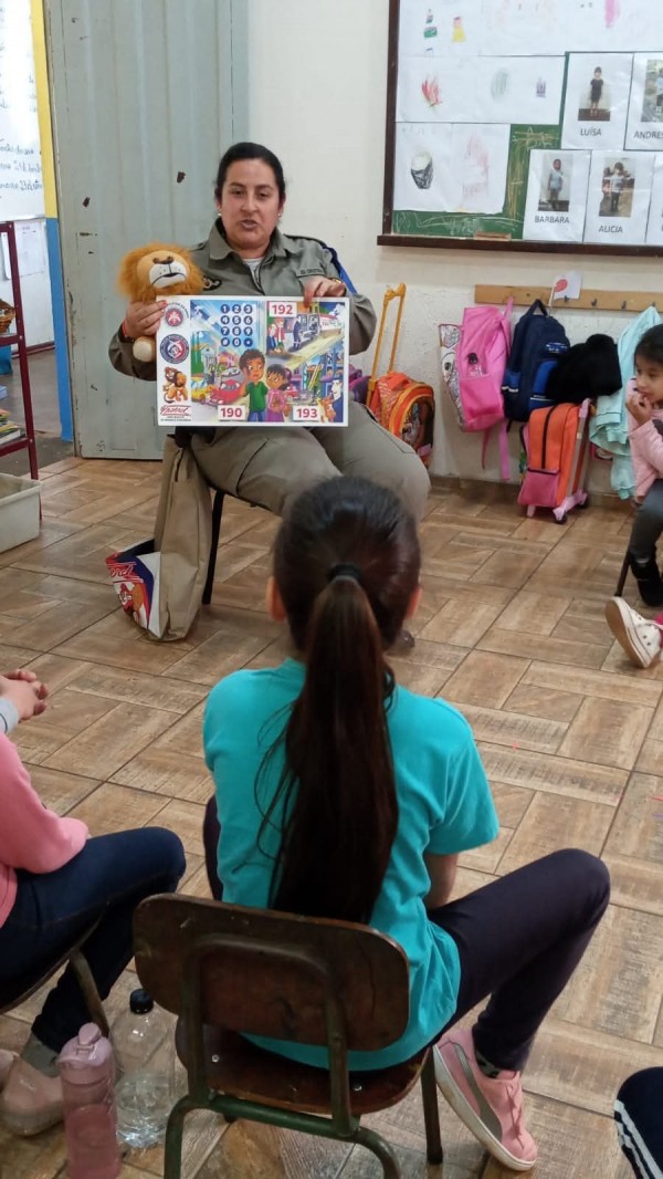 Crianças assistem a PM instrutora do Proerd contando uma história em sala de aula. 