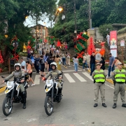 Duas duplas de PMs, uma com motocicletas e outra de prontid&atilde;o, aparecem em um local com grande presen&ccedil;a de p&uacute;blico, durante o dia, decorado com enfeites natalinos. 