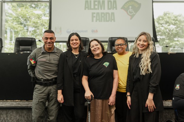 O PM aparece ao lado de quatro senhoras. Ao fundo está o palco da OAB onde aconteceu o evento e o telão do "Além da farda". 