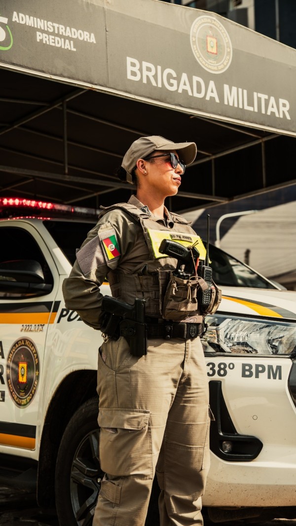 PM feminina está diante da viatura em um Posto Base da BM em um dia ensolarado. 