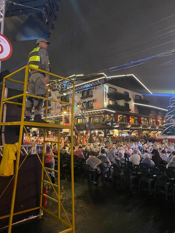 &Aacute; noite, durante um show na &aacute;rea central de Gramado, a rua est&aacute; ocupada pelo p&uacute;blico presente sentado e um PM est&aacute; sobre um pedestal, equipamento que possibilita uma visualiza&ccedil;&atilde;o panor&acirc;mica. 