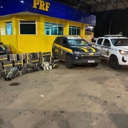 Durante a madrugada, em frente ao posto da PRF, aparecem as viaturas dessa Pol&iacute;cia e da BM. Ao lado delas, est&atilde;o as caixas que representam a grande apreens&atilde;o de maconha. 