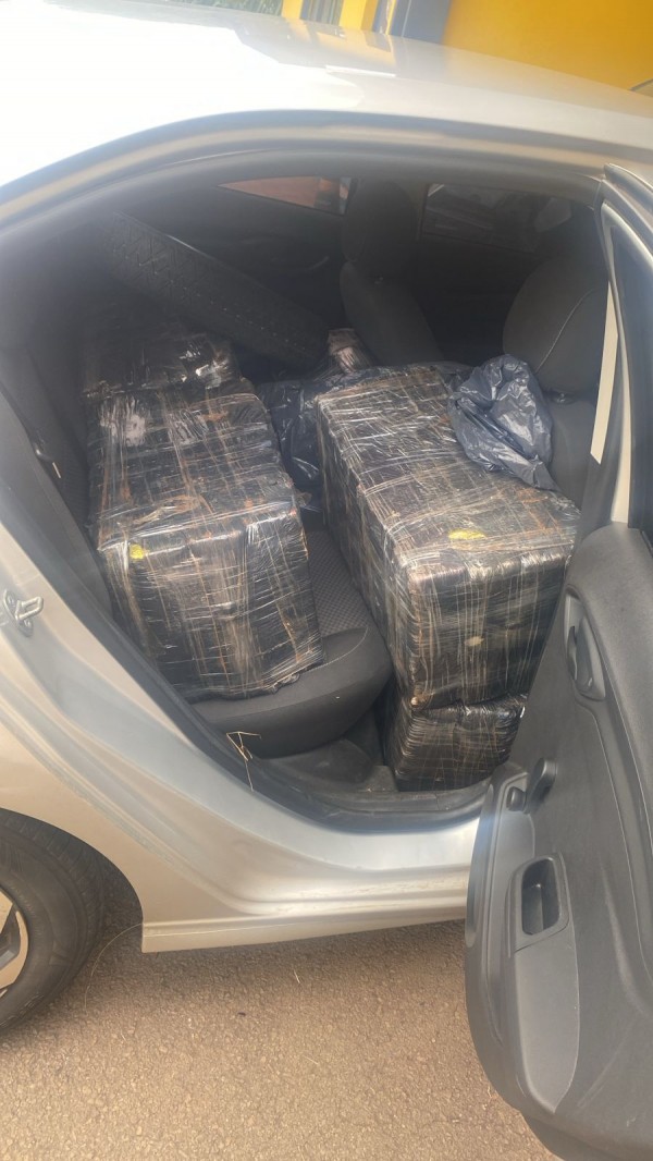 Um automóvel aparece com uma das portas traseiras abertas por meio da qual é possível ver os pacotes da droga apreendida.  