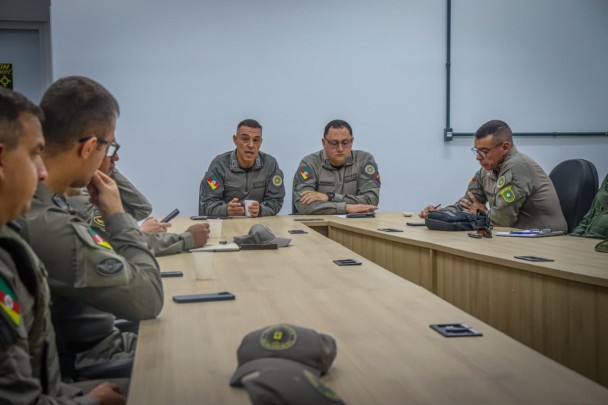 Uma grande mesa sobre a qual há bonés militares e, em volta, estão os comandantes dos efetivos que farão a segurança durante o grande evento. 
