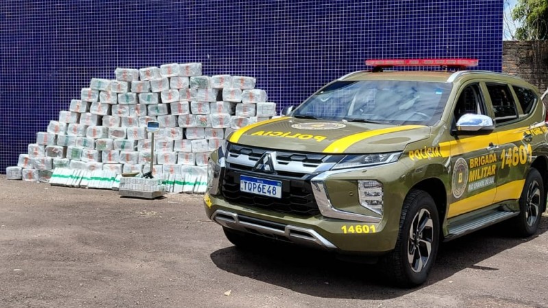Uma viatura da BM aparece ao lado da pilha em formato de pir&acirc;mide de embalagens de maconha. 