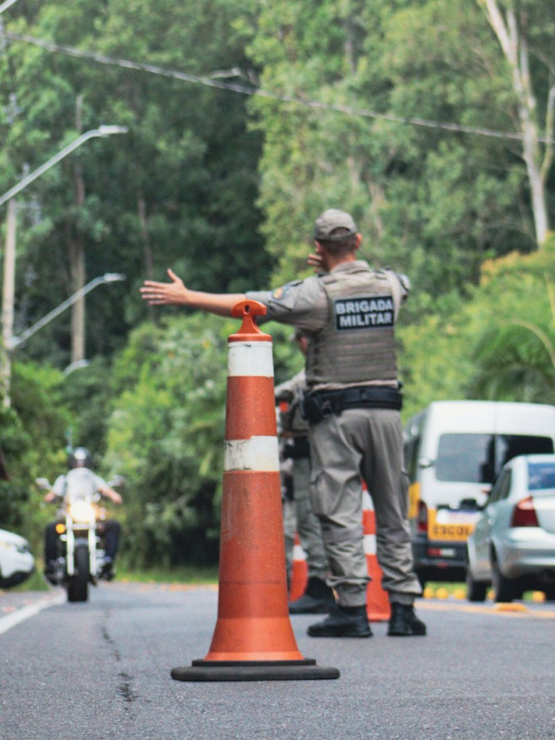 Policial Militar de costas, realizando movimento indicando ordem de parada para uma motocicleta.