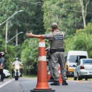Policial Militar de costas, realizando movimento indicando ordem de parada para uma motocicleta.