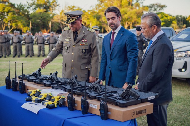 Foto mostra o comandante-geral, o governador do Estado e o secretário da Segurança Pública em frente a uma mesa com pistolas e outros novos equipamentos