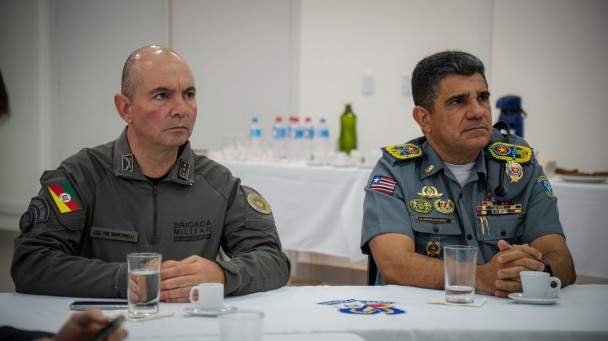 Os PMs estão sentados à mesa e acompanhando a apresentação do Sistema da BM. 