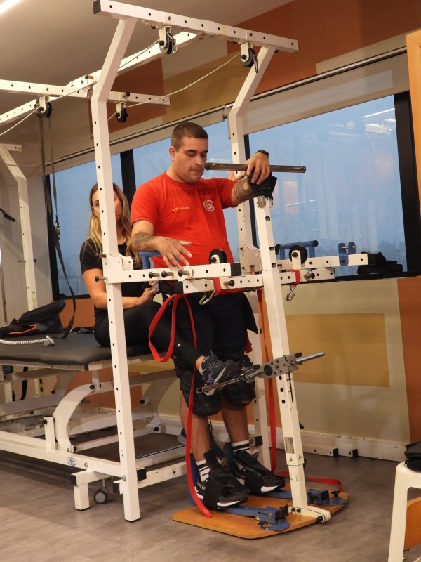 Foto mostra o soldado do Corpo de Bombeiros Giuliano em pé em um aparelho de fisioterapia