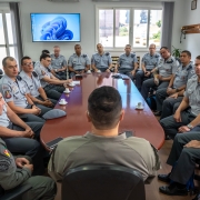 A foto mostra praticamente todos os integrantes da reuni&atilde;o da comitiva com o Comando-Geral da BM. Todos os PMs usam farda e sobre a mesa de trabalho est&atilde;o x&iacute;caras de caf&eacute; e aparelhos celulares. 