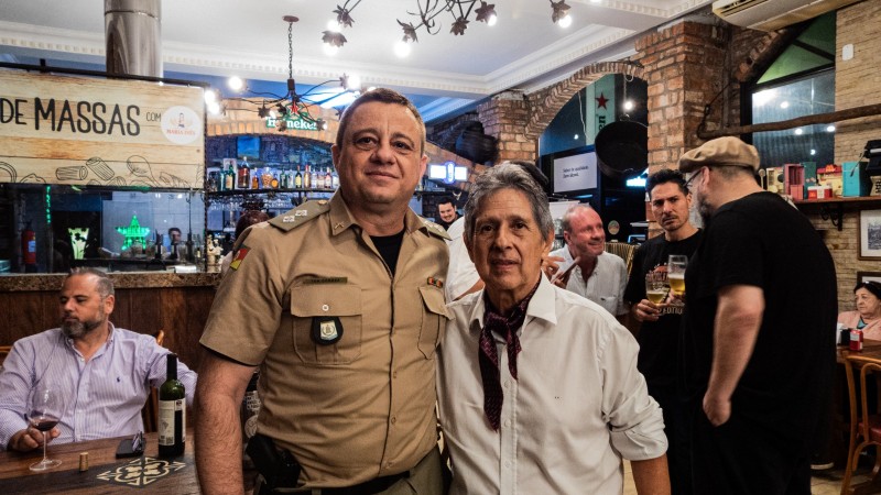 PM e artista aparecem lado a lado, no local do encontro de gaiteiros, em p&eacute; e com diversas pessoas no ambiente. 