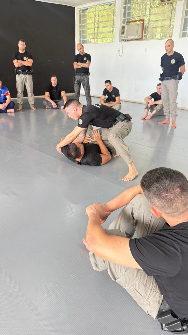 Foto mostra instrutores praticando em tatame, enquanto outros observam atentos ao redor