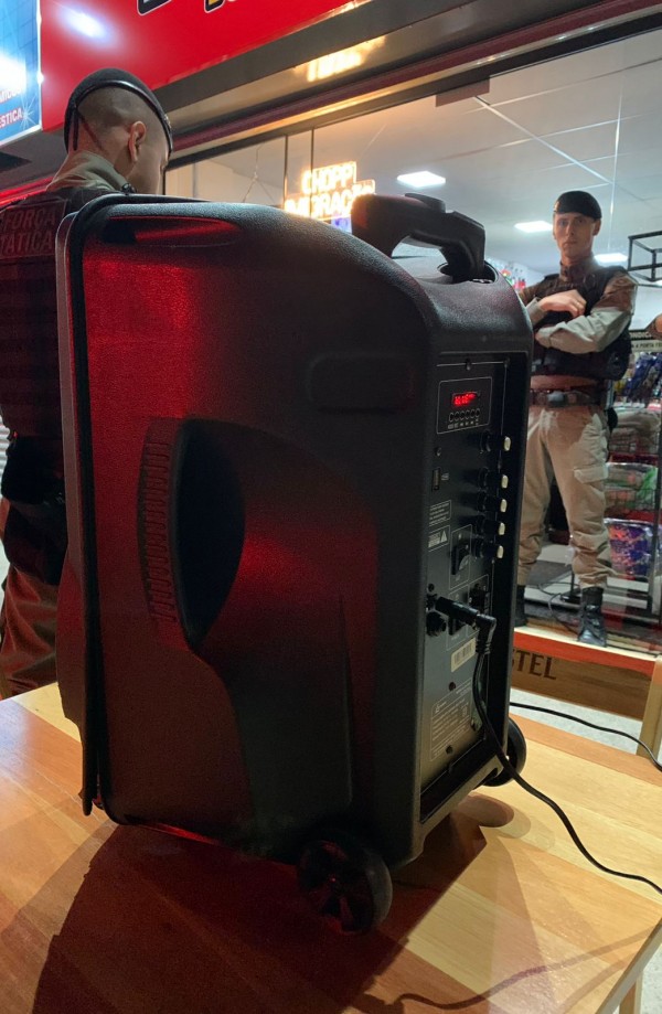 Caixa de sol aparece sobre uma mesa e, ao fundo, dois PM's em pé. 