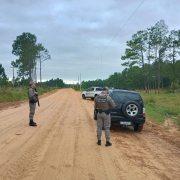 Dois PMs aparecem durante a fiscaliza&ccedil;&atilde;o de um ve&iacute;culo em uma estrada de ch&atilde;o no interior do RS. Ao fundo v&ecirc;-se uma viatura da BM. 