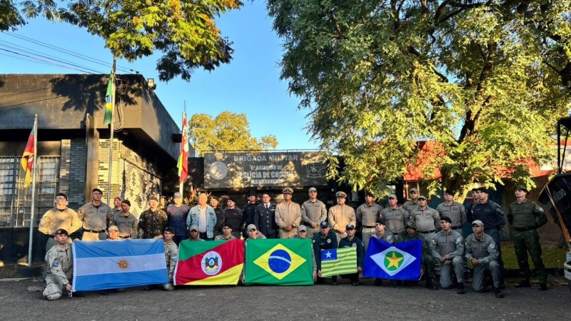 Foto mostra policiais posando para a foto, juntos. Os de fora est&atilde;o segurando as bandeiras dos seus estados ou do seu pa&iacute;s