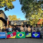 Foto mostra policiais posando para a foto, juntos. Os de fora est&atilde;o segurando as bandeiras dos seus estados ou do seu pa&iacute;s