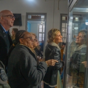 Fotografia colorida mostra um grupo de autoridades observando uma vitrine da exposição. Entre elas estão a secretária adjunta da Segurança Pública, delegada Adriana Regina da Costa, o coronel da reserva remunerada Jerônimo Carlos Santos Braga e policiais militares. Todos observam atentamente os materiais expostos no Museu da Brigada Militar.