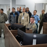 Grupo de participantes observa demonstração do sistema da Brigada Militar em sala de monitoramento do COPOM