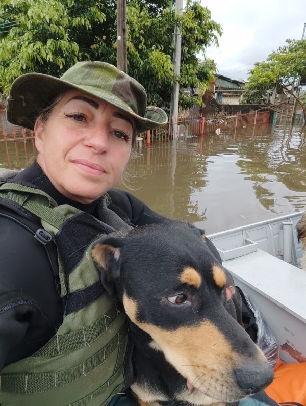 A PM aparece em uma selfie, fardada, segurando um cão resgatado dentro de um barco em meio a água que ocupou bairros no período da enchente que acometeu o RS em 2024. 