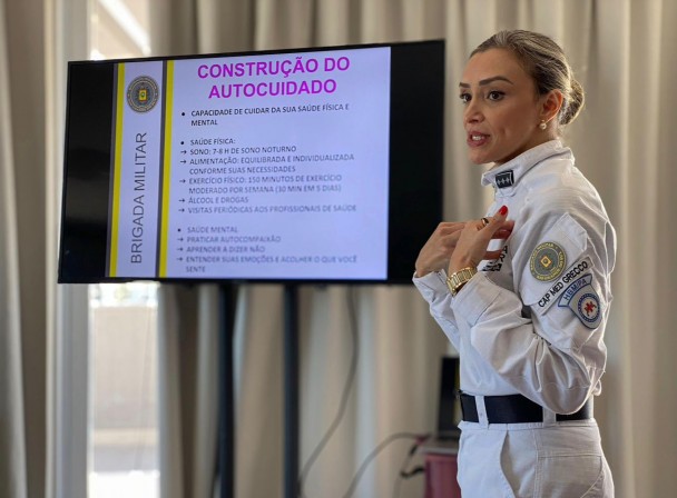 PM aparece fardada durante uma palestra para a tropa. Ao fundo, vê-se um slide que aborda o autocuidado. 