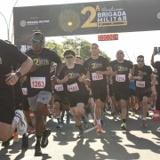 Imagem mostra o momento de in&iacute;cio do percurso. Aparecem os participantes correndo vestindo as camisetas da prova. Ao fundo, aparece o p&oacute;rtico com cron&ocirc;metro da corrida. 