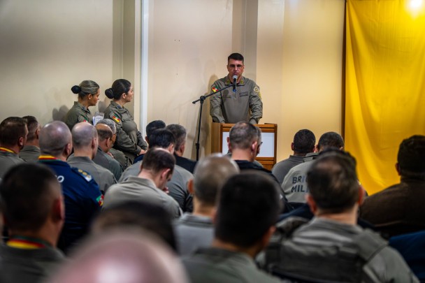 A imagem mostra o diretor do Departamento de Pessoal e Finanças, coronel PM Cléber Rodrigues dos Santos, em pé atrás de um púlpito realizando seu pronunciamento. Militares estaduais acompanham a fala sentados no auditório.