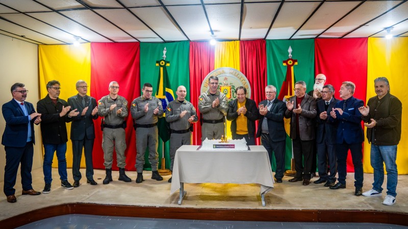 Grupo de autoridades e convidados em p&eacute;, no palco, aplaude ao redor de uma mesa com bolo comemorativo dos 28 anos do DPF.