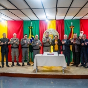 Grupo de autoridades e convidados em p&eacute;, no palco, aplaude ao redor de uma mesa com bolo comemorativo dos 28 anos do DPF.