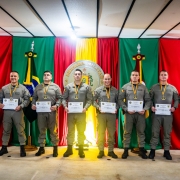 Policiais militares fardados posam no palco com diplomas e medalhas recebidos durante a cerimônia comemorativa do DPF.