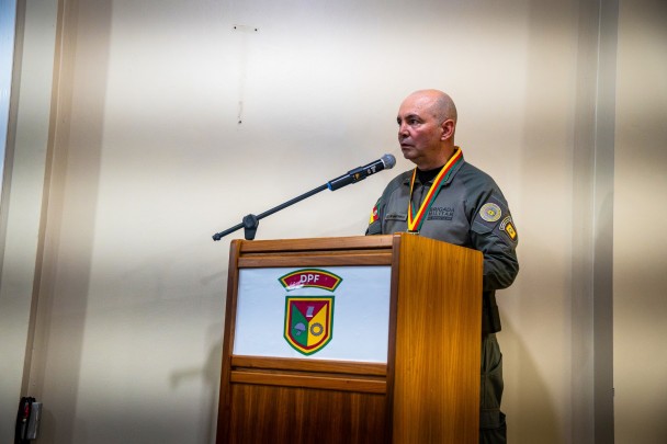 Oficial da Brigada Militar, usando farda e medalha, discursa ao microfone atrás de um púlpito com o símbolo do DPF.