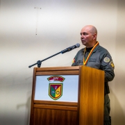 Oficial da Brigada Militar, usando farda e medalha, discursa ao microfone atrás de um púlpito com o símbolo do DPF.