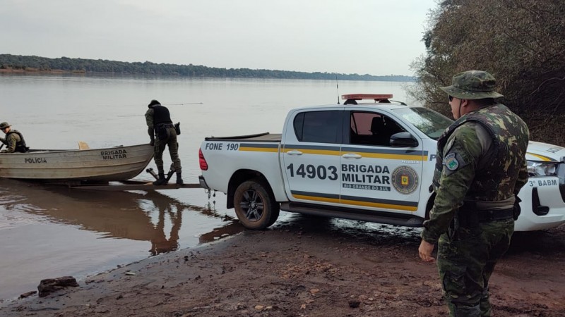 PMs do Comando de Pol&iacute;cia Ambiental est&atilde;o junto a uma viatura na beira de um curso d'&aacute;gua onde est&aacute; um barco com um PM dentro. 